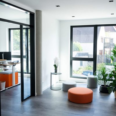 Blick in eine Sitzecke mit runden Sitzkissen und in ein angrenzendes Büro von B2 Steuern
